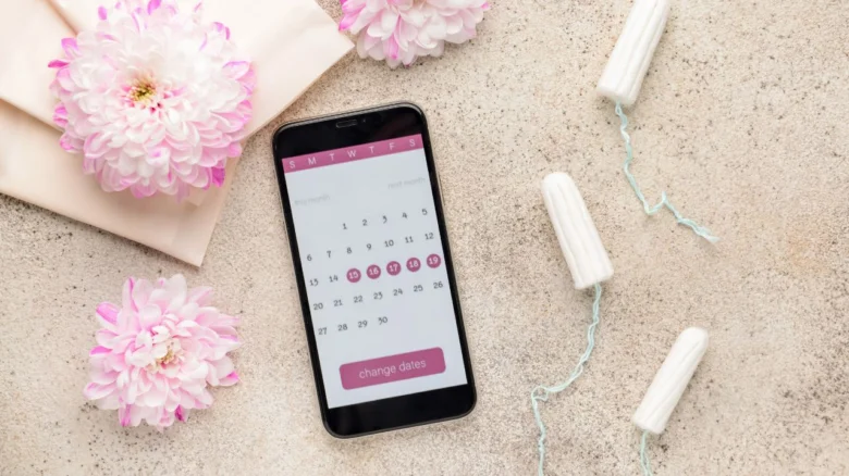 Telefon s kalendářem menstruačního cyklu, vataky a květy.