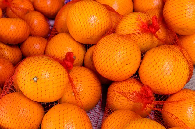 Mandarinky v červených síťových pytlích na plném záběru.