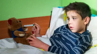 Chlapec leží v posteli s teploměrem a hračkou.
