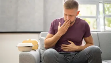 Muž sedí na gauči s bolestmi břicha po jídle.