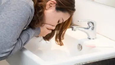 Žena se naklání nad umyvadlo s příznaky zvracení.