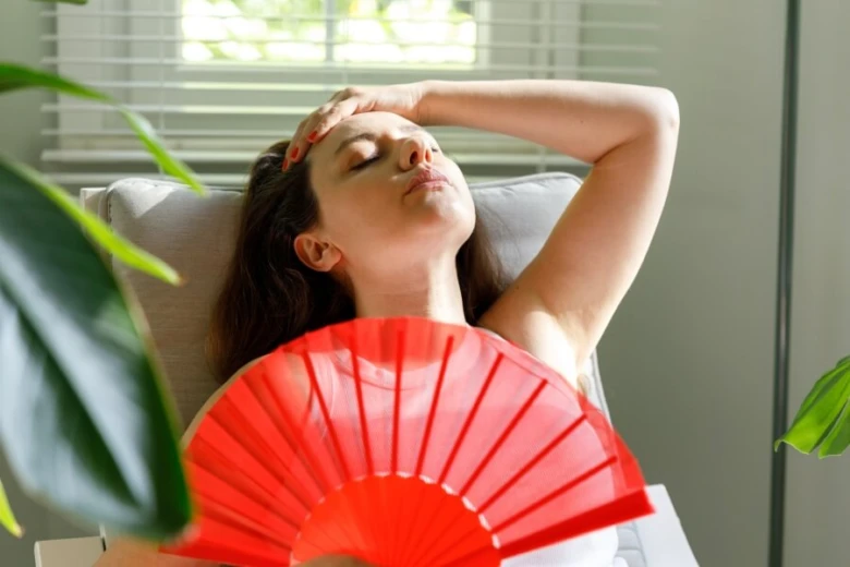 Žena se větrá červeným ventilátorem kvůli přehřívání organismu.