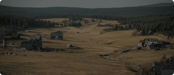 Venkovská krajina s domy v údolí obklopeném lesy.