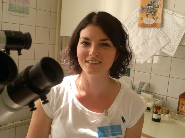 Žena v bílé košili s identifikačním štítkem u oftalmologického vybavení.
