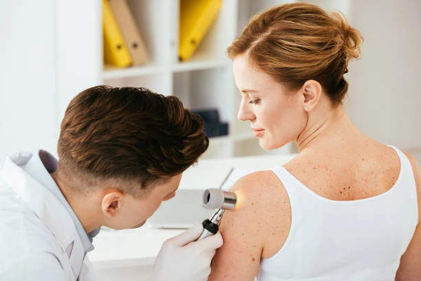 Dermatolog zkoumá pacientovu kůži pomocí dleroskopu.