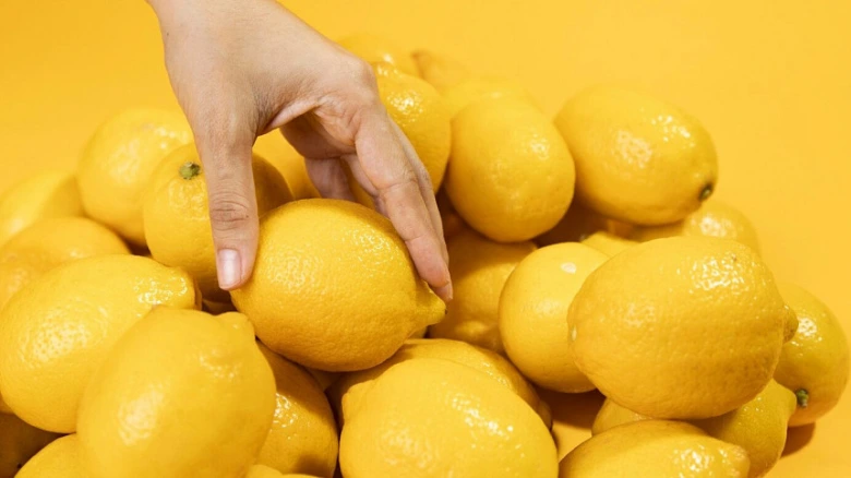 Ruka vybírá čerstvý citron z hromady žlutých plodů.