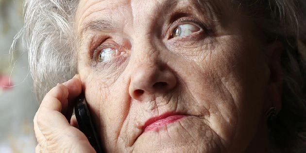 Starší žena na telefonu s výrazem zmatení, typickým pro Alzheimerovu chorobu.