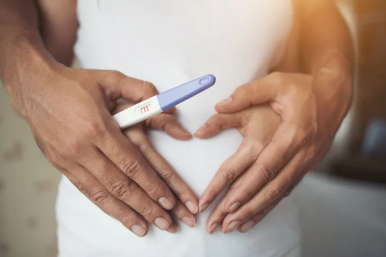 Muž drží těhotenský test nad břichem po pozitivním výsledku.