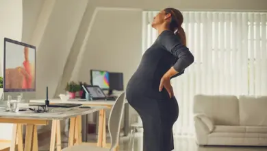 Těhotná žena drží si bedra v kanceláři kvůli bolesti zad.