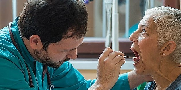 Lékař vyšetřuje hrdlo pacienta pomocí nástroje.
