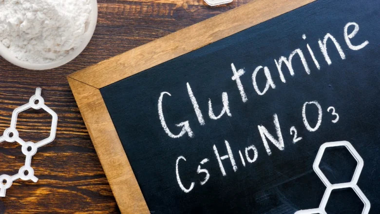 Malá miska bílého prášku l-glutaminu vedle tabule s chemickým vzorcem.