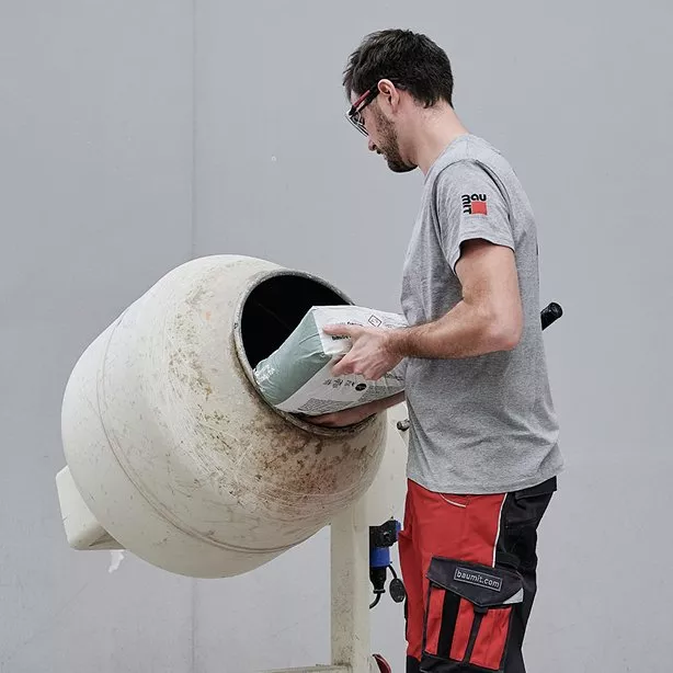 Muž nalévá beton z pytli do betonu smíchavače.