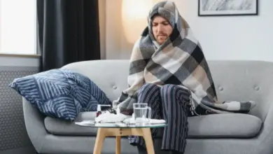 Muž zabalený v dečce sedí na gauči s příznaky nemoci.