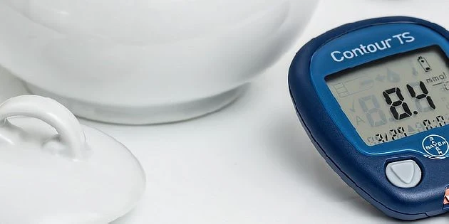 Modrý glukometr s výdisplejem vedle bílé misky pro diabetika.