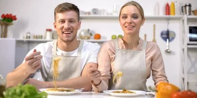 Muž a žena jedí těstoviny v kuchyni.