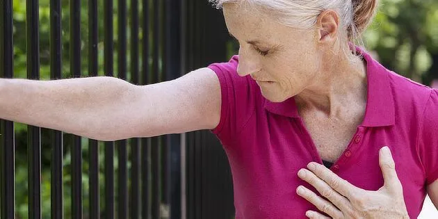 Žena se drží za hrudník v bolesti při angině pectoris.