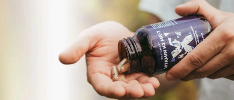 Ruce s lahvičkou vitamínu K2 MK-7 a tobolky v dlani.