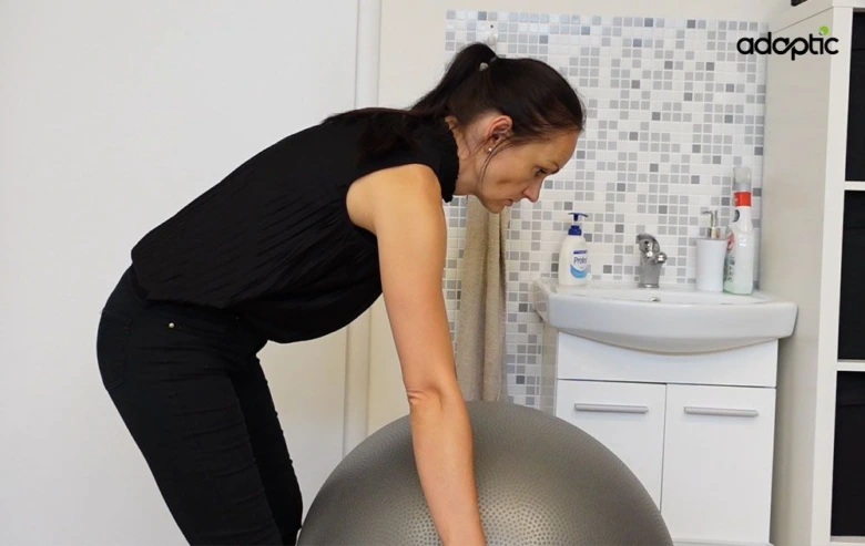 Žena cvičí s velkou gymnastickou koulí pro úlevu od bolesti zad.