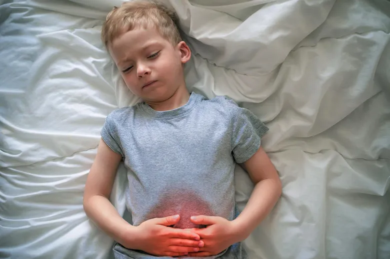 Dětský chlapec leží v posteli a drží si břicho kvůli průjmu.