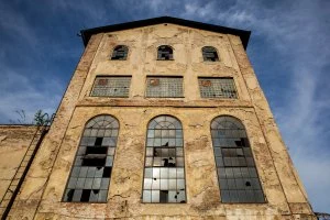 Historická budova lihovaru Smíchov s velkými okny pod modrou oblohou.